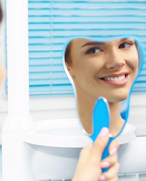 Dental patient using mirror to admire results of her recontouring procedure