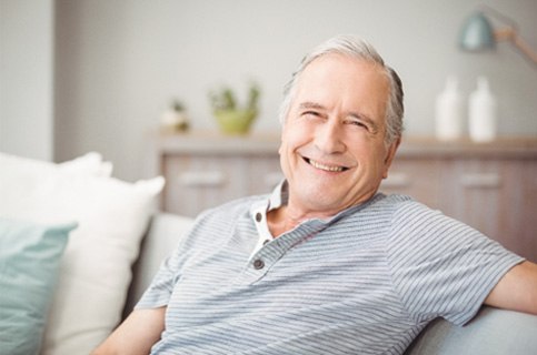 Man sitting on couch smiling with dental implants in Dallas, TX
