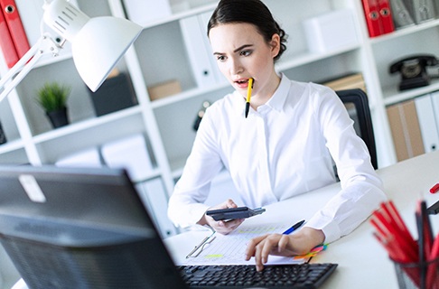 A young female chews on a pen while working on her computer in Dallas