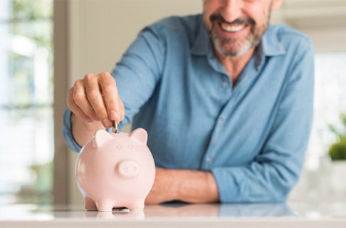 Someone smiling and putting money in a piggy bank