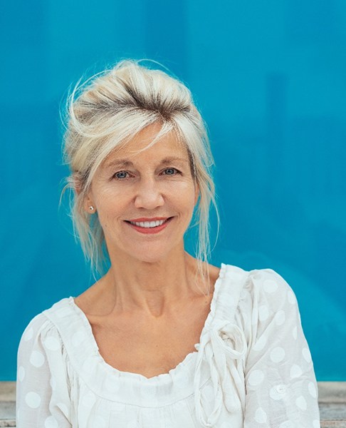 Woman in white shirt enjoying benefits of implant dentures