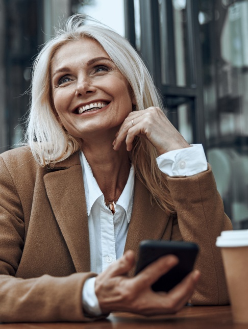 Smiling woman holding her cell phone while sitting at table